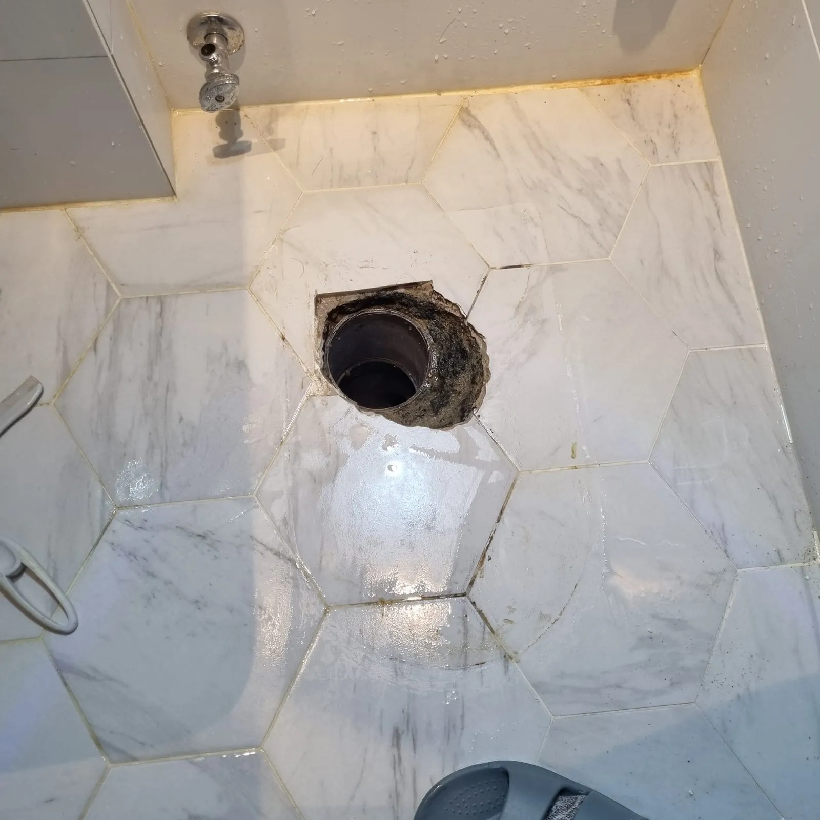 오물이 닦인 타일 바닥 한가운데에 배관 입구가 열려 있고, 입구 둘레 가장자리에 검은 때가 남아 있다
